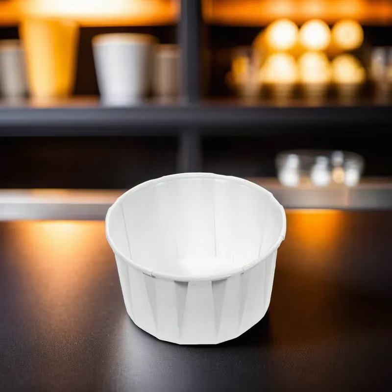 White compostable condiment cup on a dark surface with blurred shelves in the background