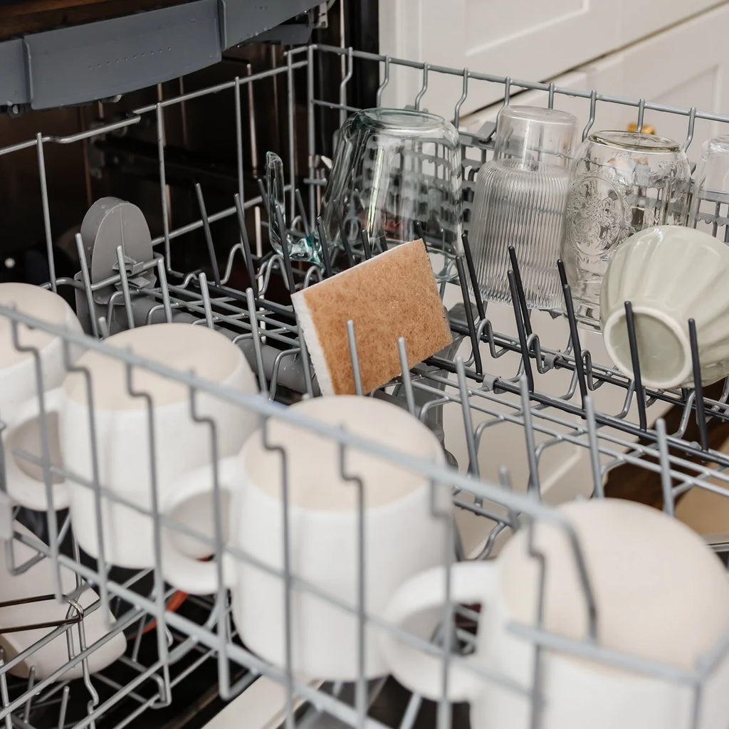 Dishwasher rack with a disinfected sponge, clean dishes, including cups, bowls, and a cutting board.