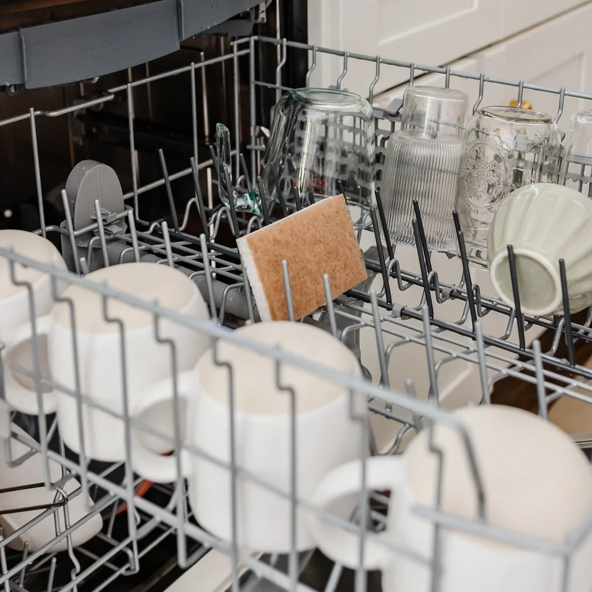 Dishwasher rack with a disinfected sponge, clean dishes, including cups, bowls, and a cutting board.