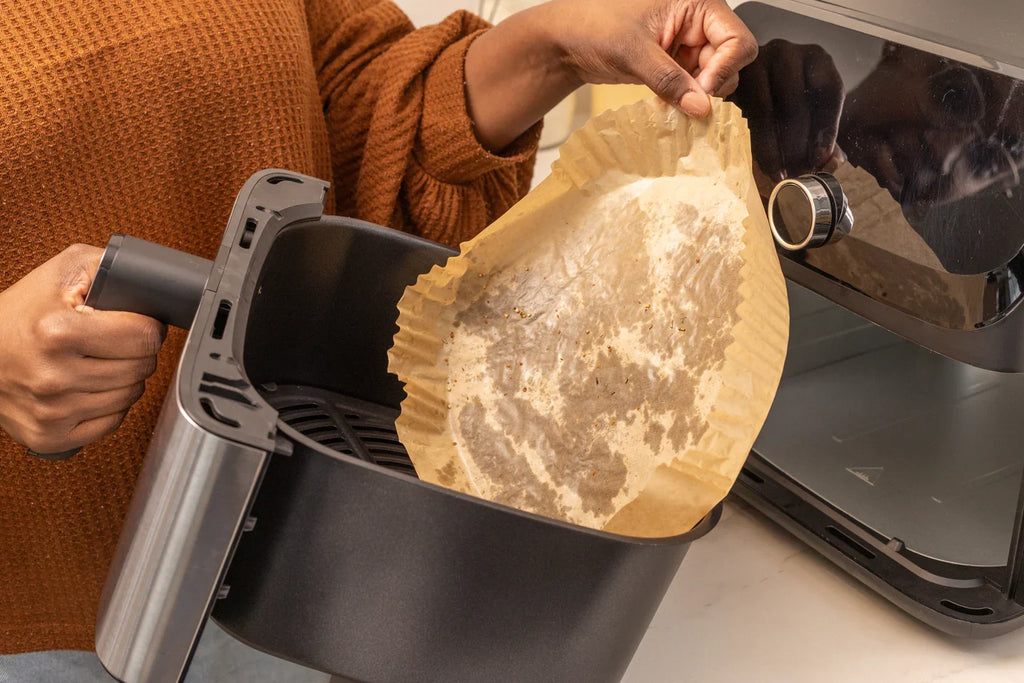 Person holding an air fryer basket with a compostable liner that has been used.