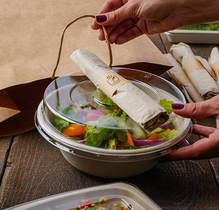 Rolled cutlery set on top of a takeout bowl with lid.