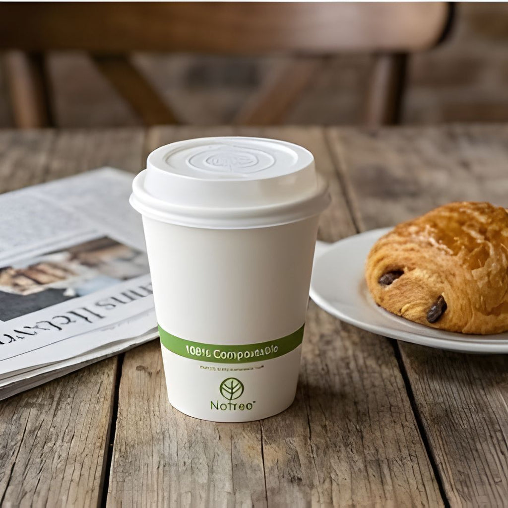 Compostable coffee cup with a compostable lid and a croissant on a wooden table