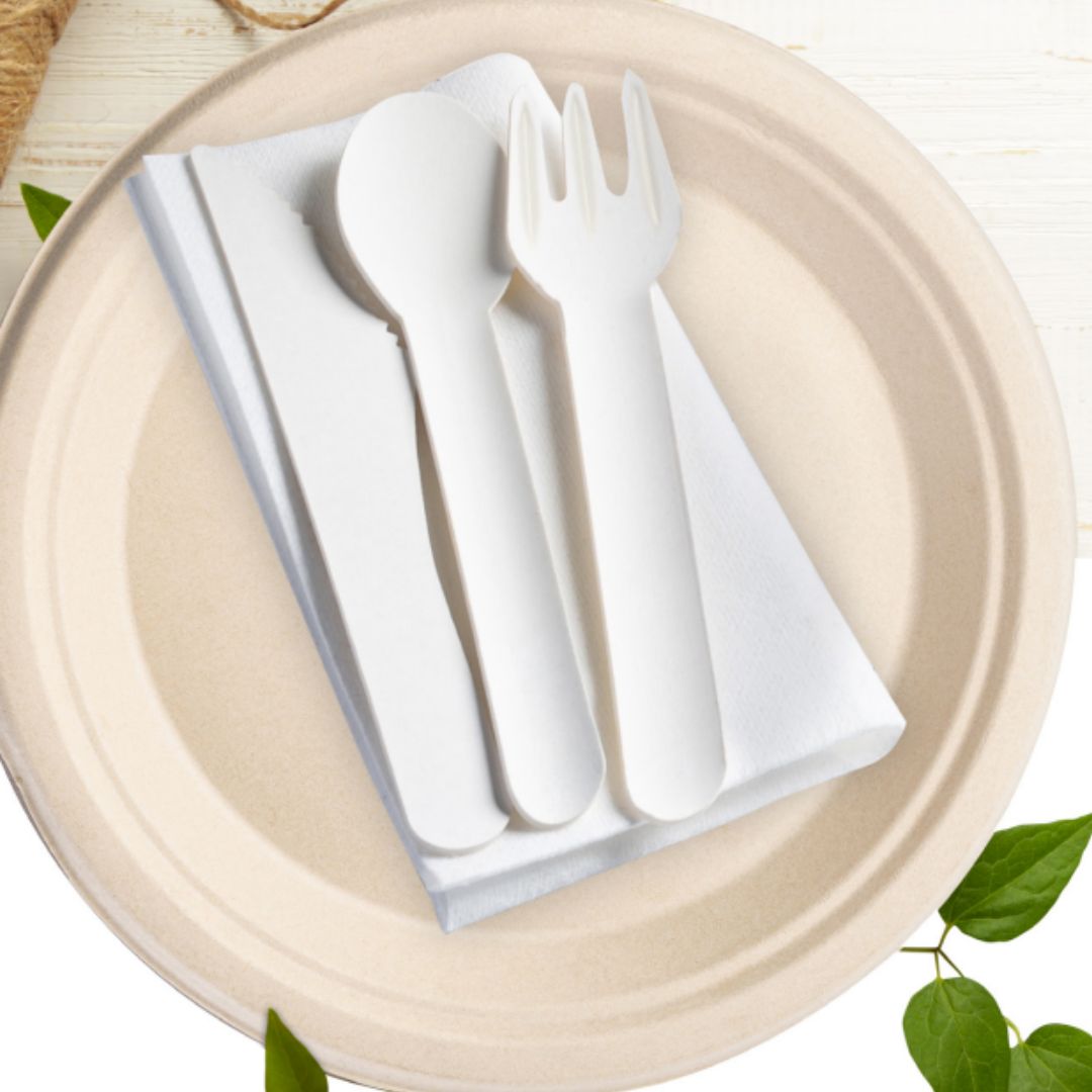 White paper cutlery set on a beige plate with green leaves in the background
