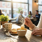 Person eating soup from a bowl with a spoon at a table in a cafe.