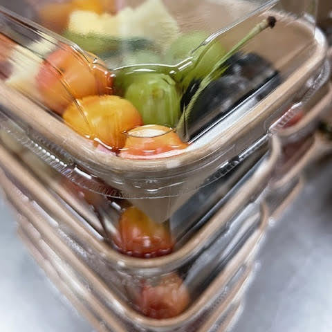 Packaged fruits, including apples and grapes, are visible through a clear plastic container.