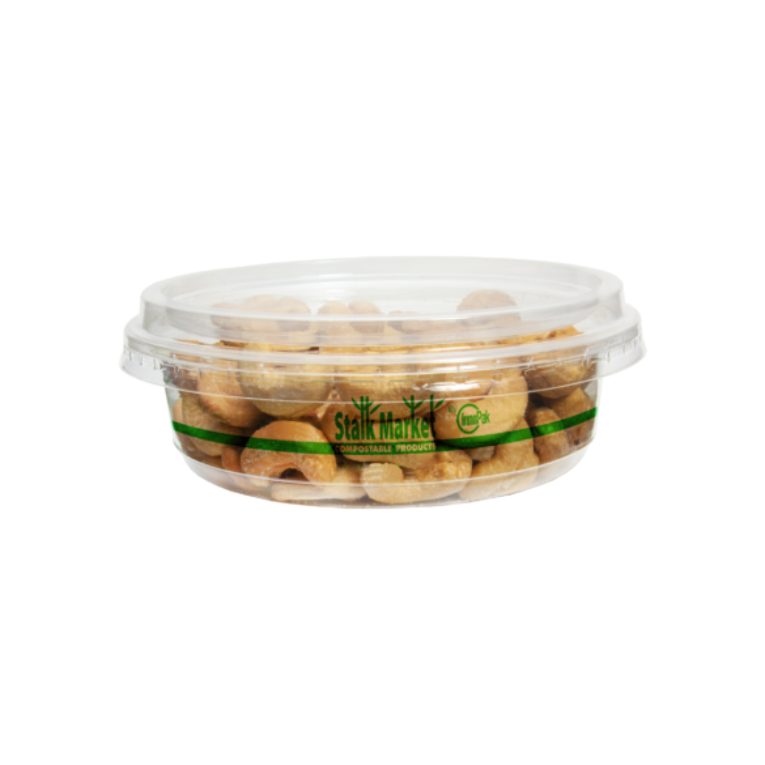 Deli container with lid filled with cashews on a plain background.