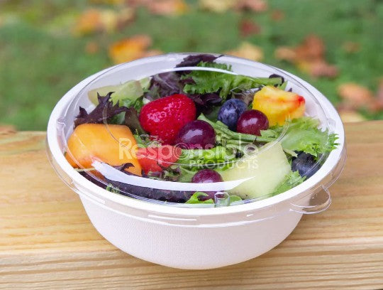 Salad with fruits and vegetables in a white bowl with a plastic lid on a wooden surface.