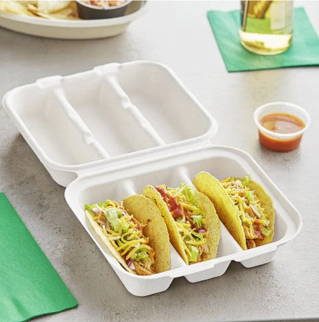 White takeout taco clamshell with tacos on a gray surface with a green napkin and glass in the background.