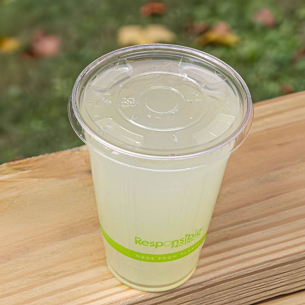 Clear plastic cup with lid on a wooden surface, blurred greenery in the background