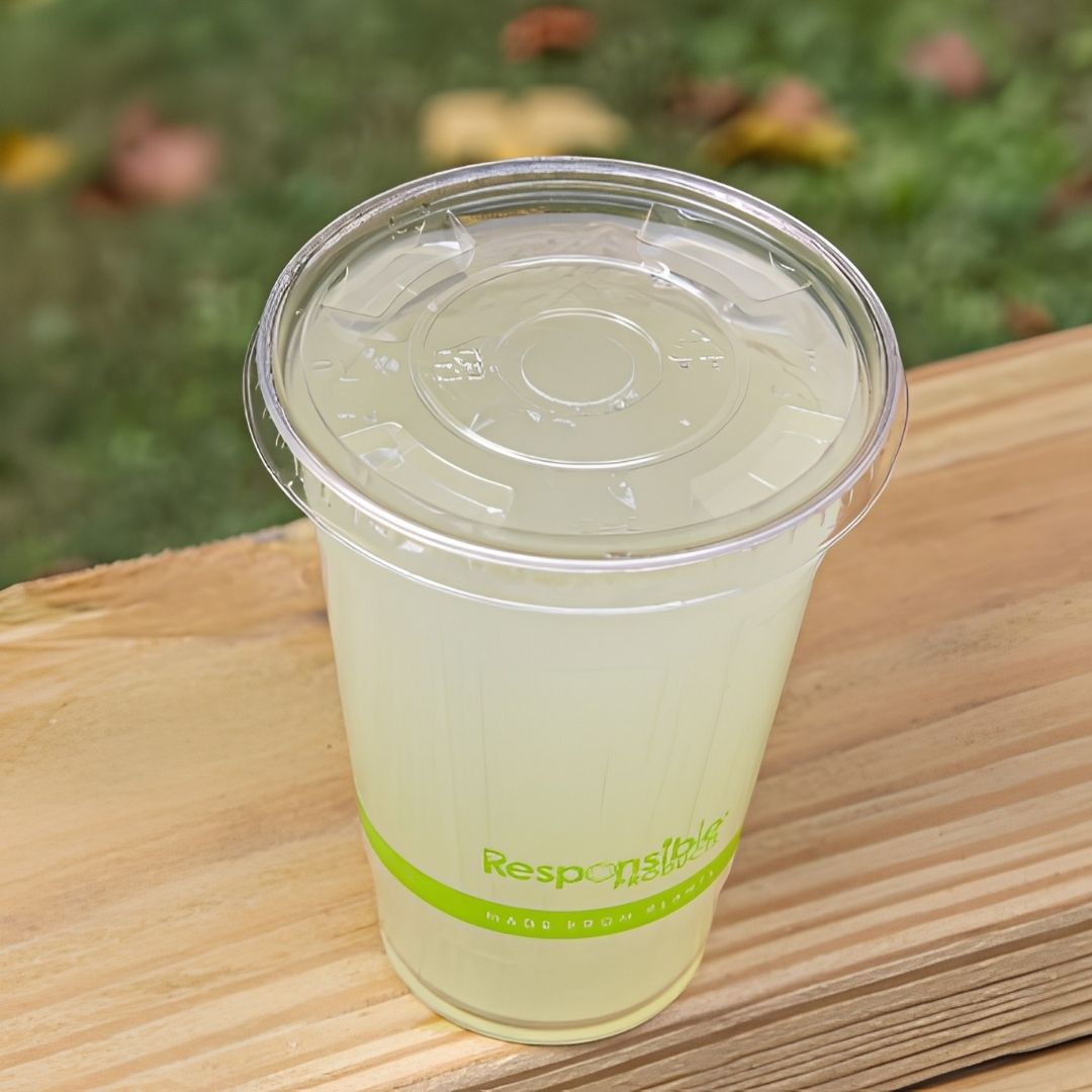 Clear plastic cup with lid on a wooden surface, blurred greenery in the background