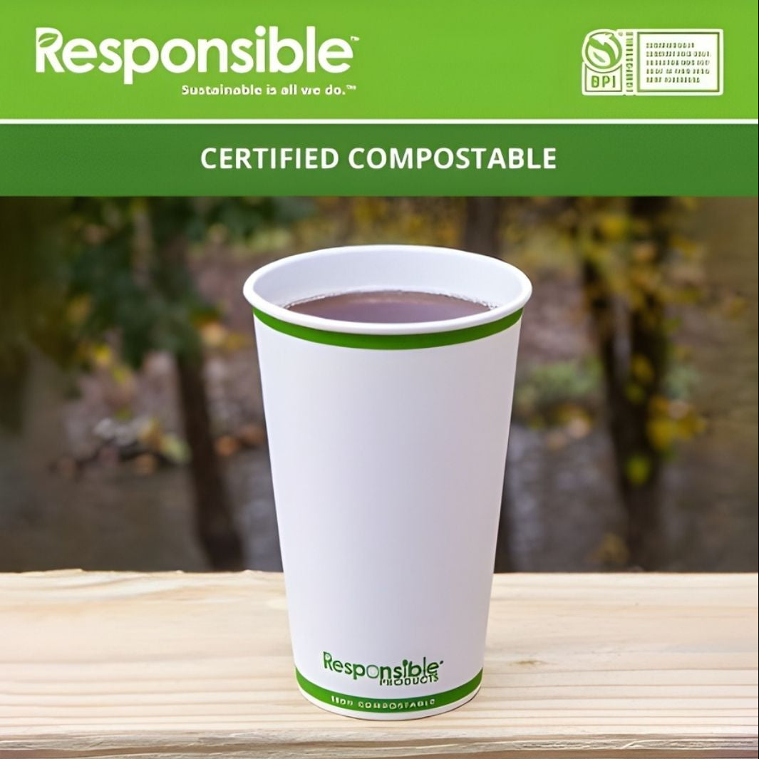 White compostable cup with green rim on a wooden surface, branded 'Responsible', with a blurred natural background.