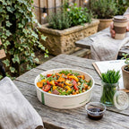 Salad bowl on a wooden table with plants and a coffee cup in the background
