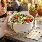 Hand holding a bowl of salad with visible ingredients on a wooden table.