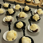 Multiple small bowls with compostable spoons of ice cream on a gray surface.