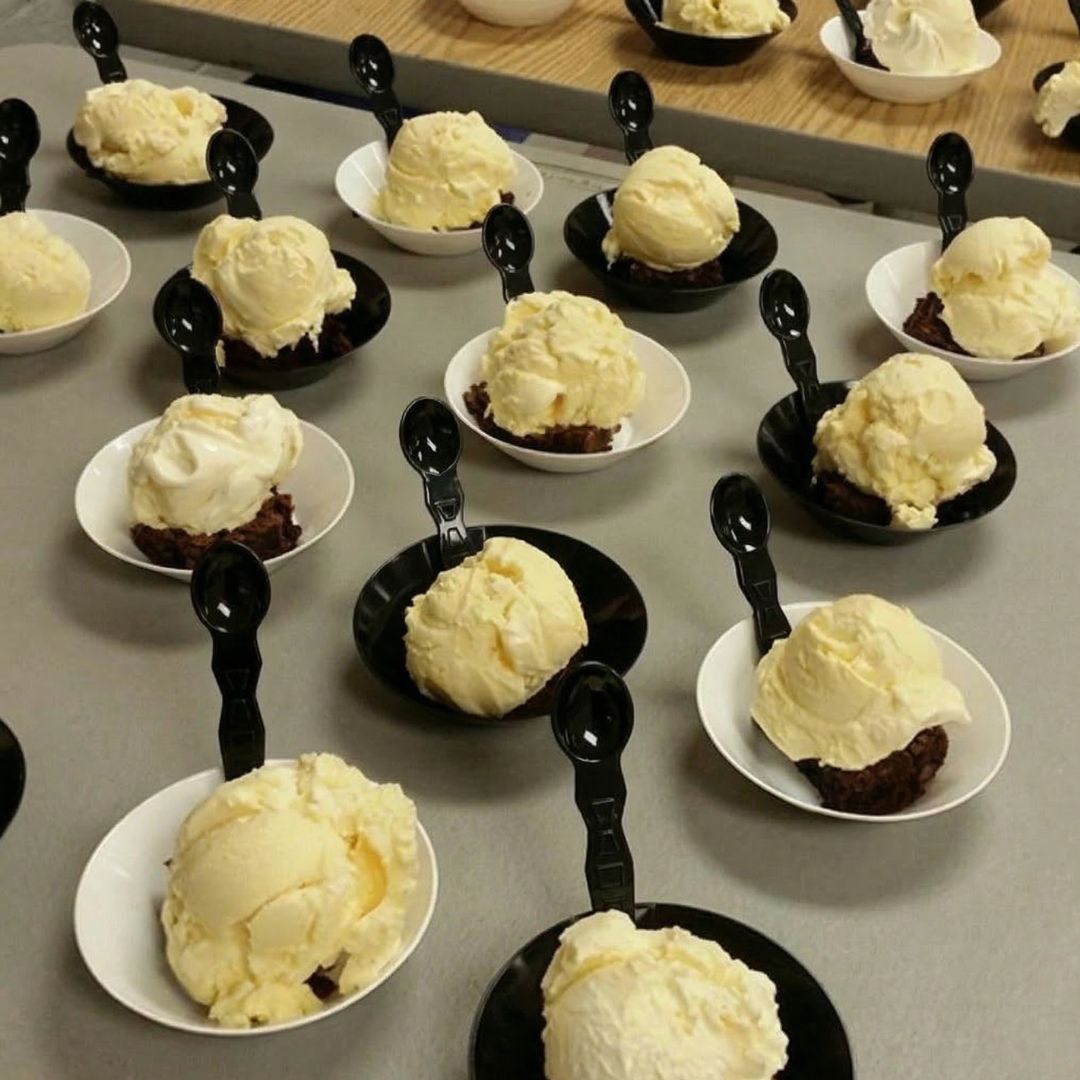 Multiple small bowls with compostable spoons of ice cream on a gray surface.