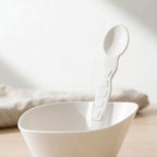 White compostable bowl with a matching taster spoon on a light background
