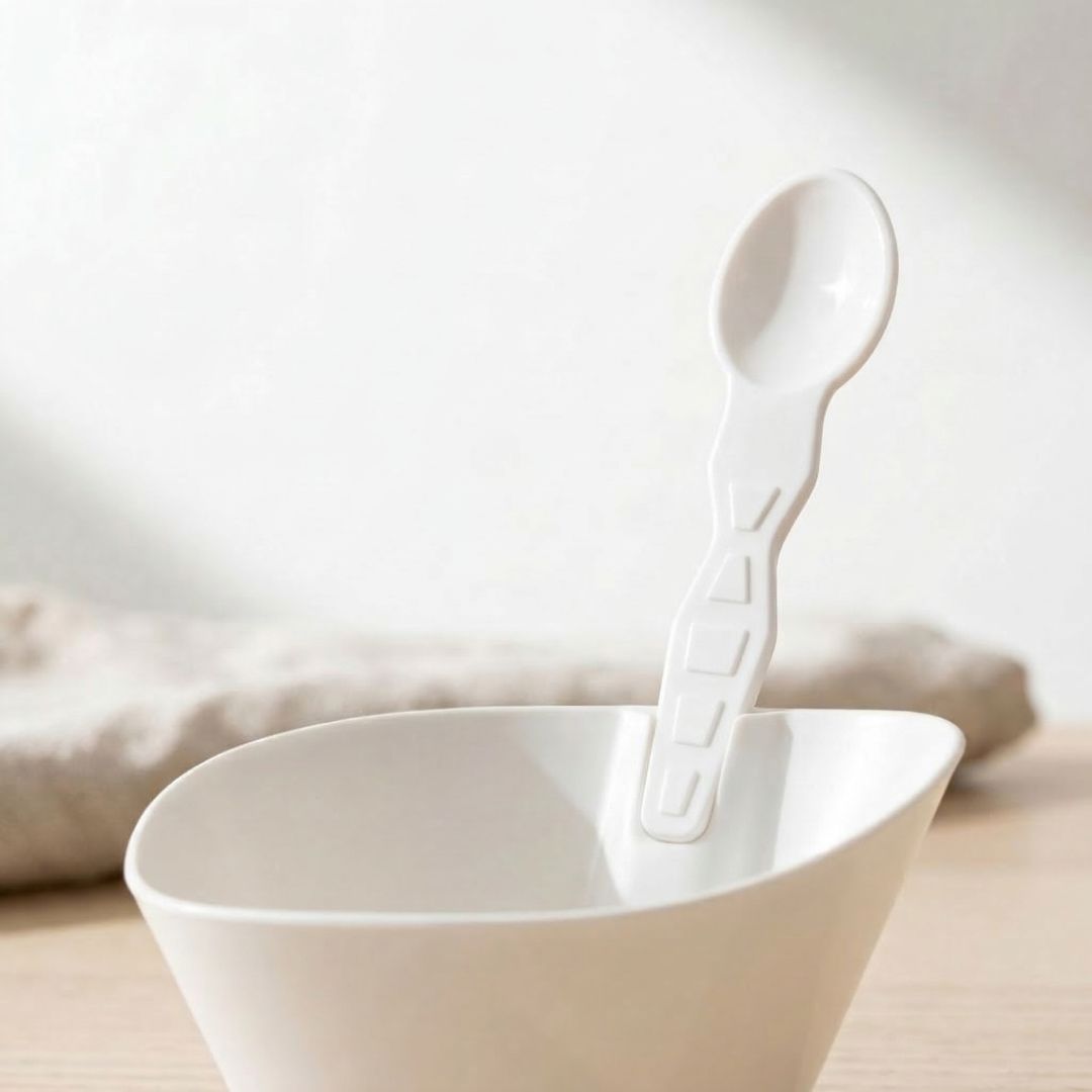 White compostable bowl with a matching taster spoon on a light background