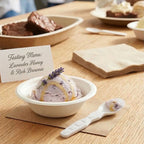 Bowl of lavender honey ice cream with a taster spoon on a wooden table, featuring a 'Tasting Menu' card.