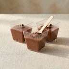 Three small clear containers filled with chocolate mousse on a light surface.
