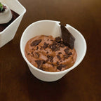 Chocolate ice cream with chocolate shavings in a compostable white cup on a brown surface
