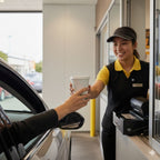 Person receiving a coffee from a drive-thru employee at a fast-food restaurant.