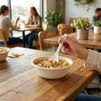 Person holding a compostable soup spoon over a bowl of soup in a restaurant setting