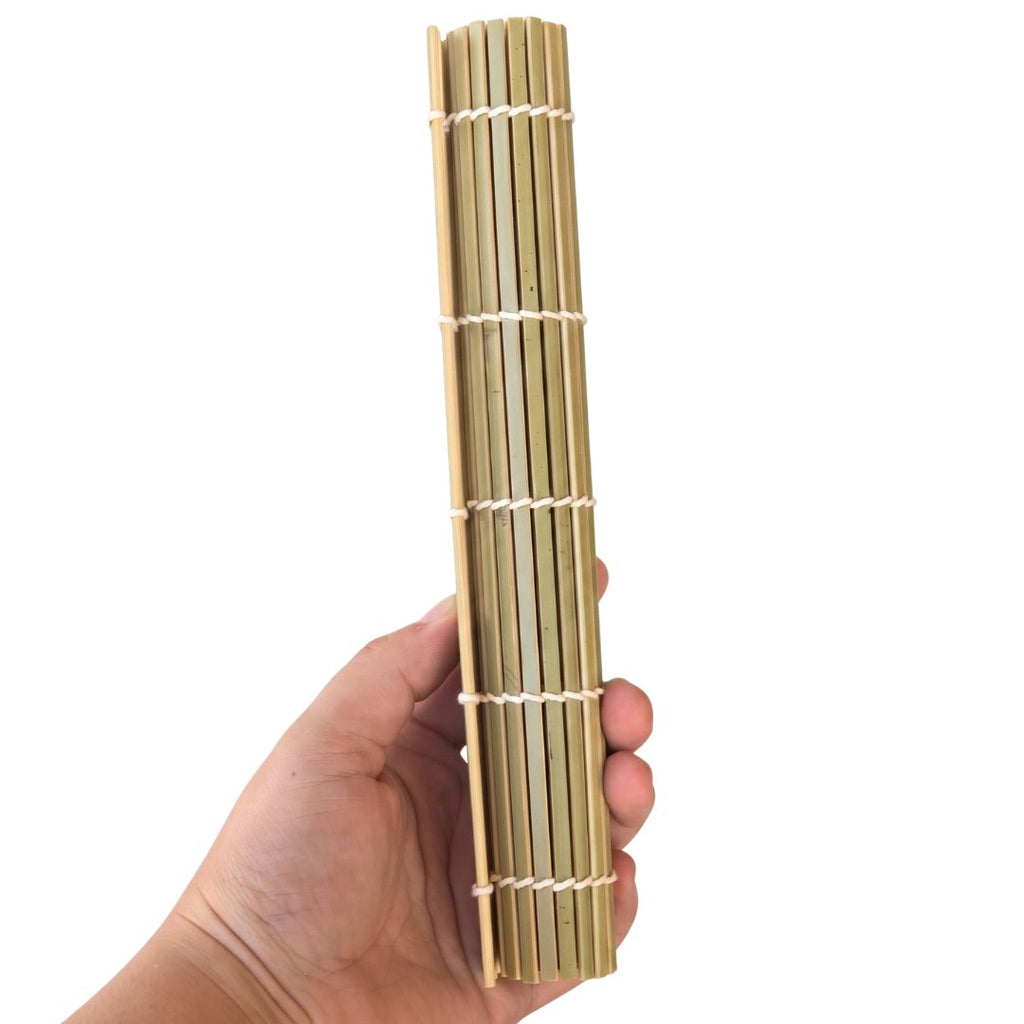 A hand holding a rolled-up bamboo sushi mat against a plain white background.