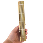 A hand holding a rolled-up bamboo sushi mat against a plain white background.