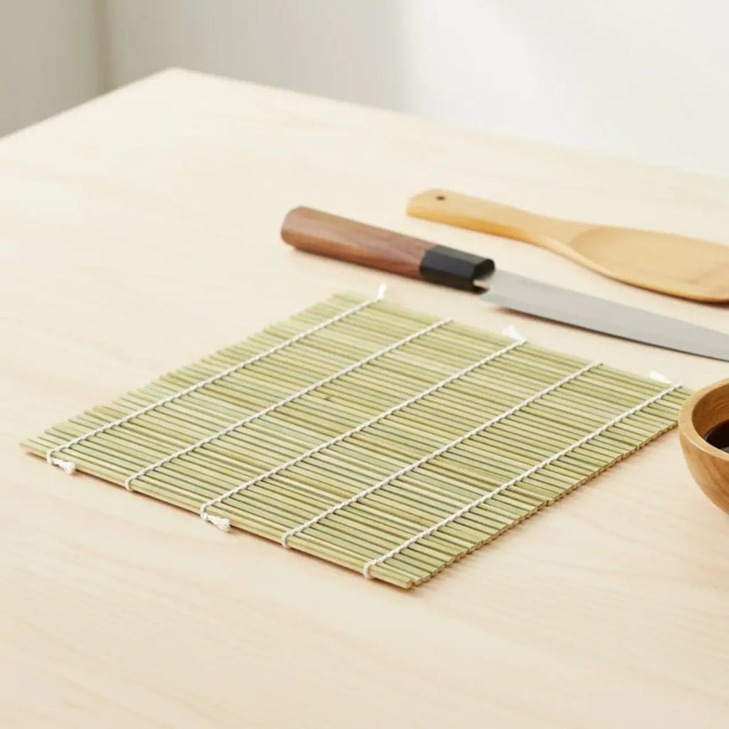 Sushi rolling mat with a knife and other tools on a light surface