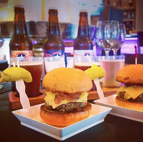 Burgers on small compostable plates with drinks in the background