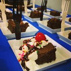 Chocolate brownie dessert with whipped cream and a cherry on top, served with on a square white plate.
