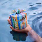 Colorful roll of toilet paper held over water with a person's hand