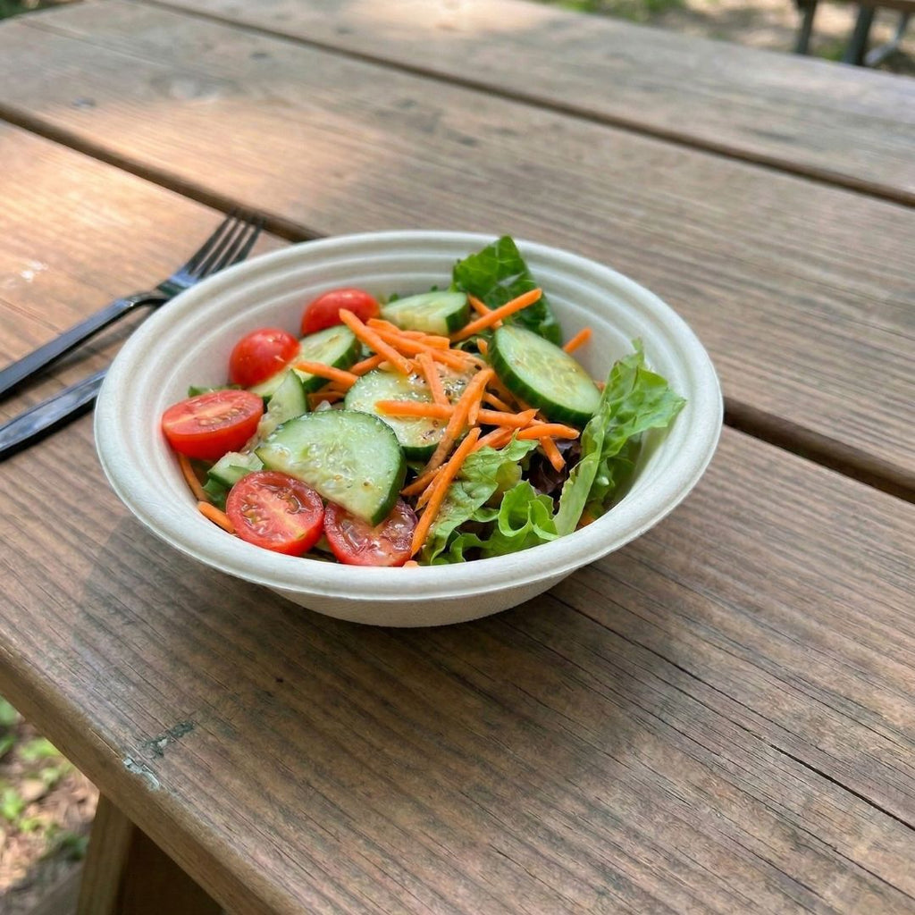 Compostable fiber bowl of salad with cucumbers, carrots, and tomatoes on a wooden table