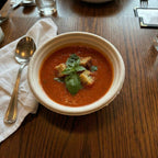 Tomato soup with croutons and basil in a beige bowl on a wooden table.