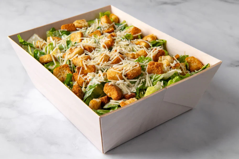 Caesar salad with croutons and cheese in a wooden tray on a marble surface