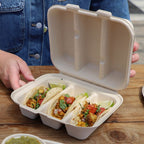 Open compostable food container with three tacos on a wooden table.