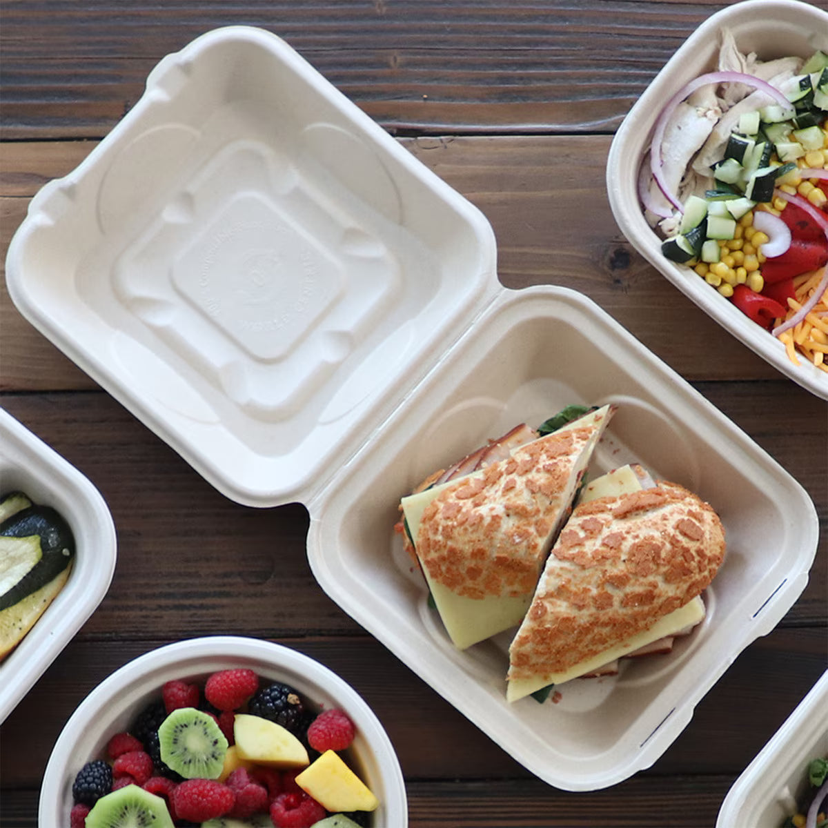 Take-out clamshells with sandwiches and salads on a wooden table