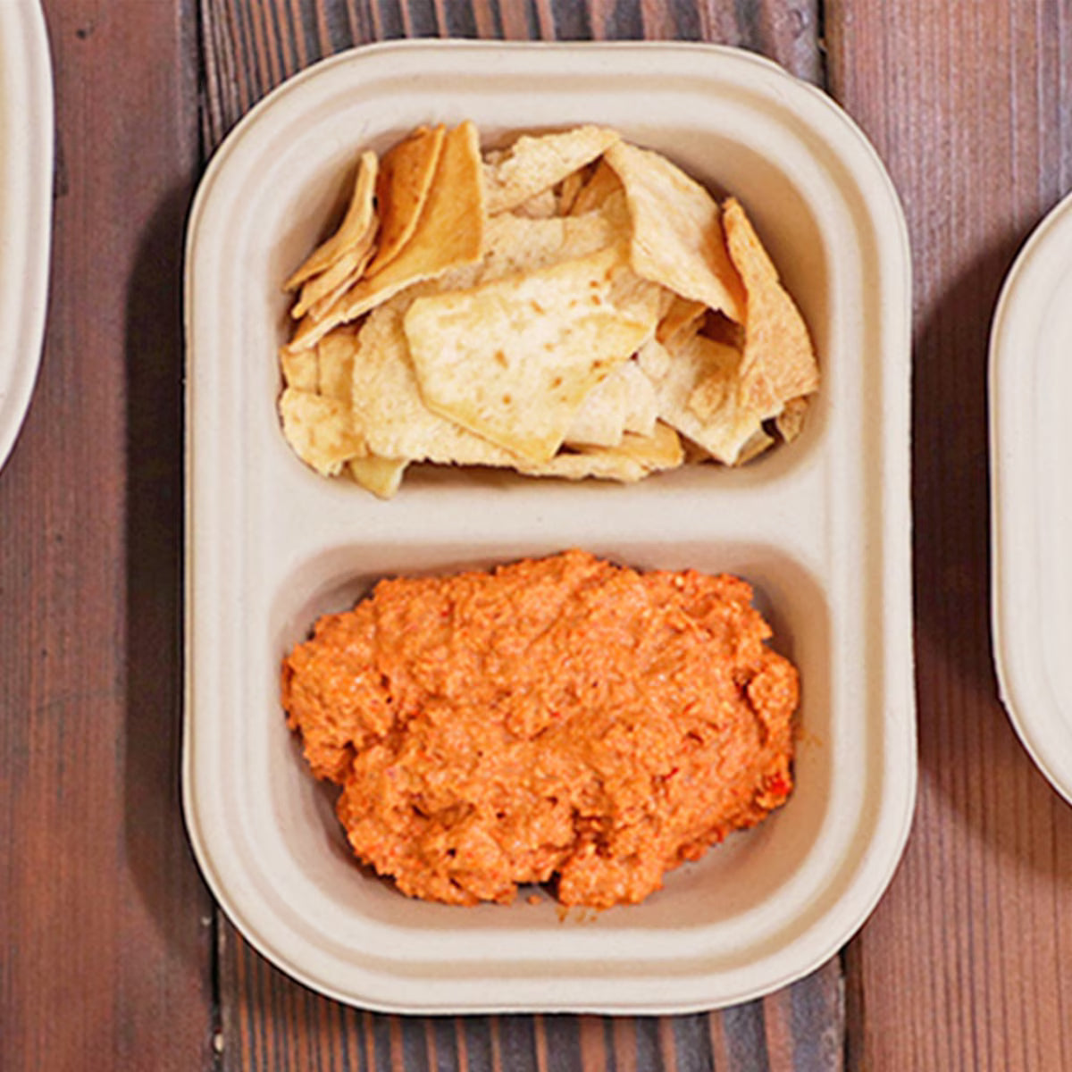Container with tortilla chips and a red sauce on a wooden surface