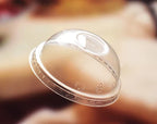 A clear dome lid with a ridged rim, shown floating against a heavily blurred warm brown background.