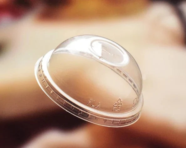 A clear dome lid with a ridged rim, shown floating against a heavily blurred warm brown background.