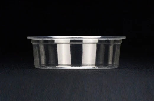 A clear portion cup on a dark textured surface against a black background.