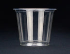 A compostable portion cup with a flared rim, shown on a dark textured background.