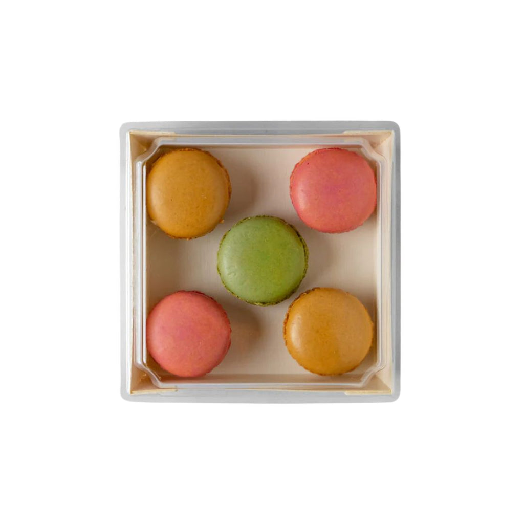 Five colorful macarons in a small wooden box with a lid on a white background