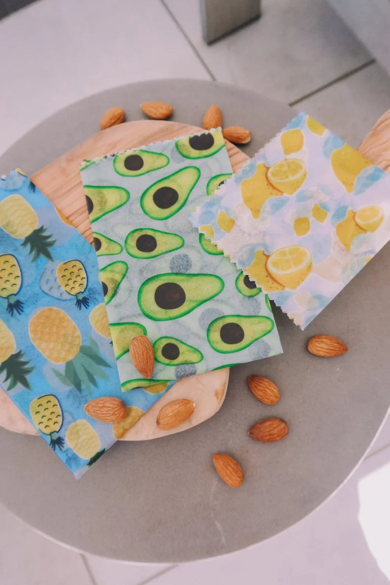Three reusable wax wraps with fruit patterns on a gray surface.