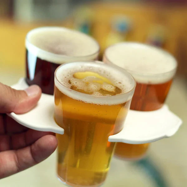 Three compostable cups of beer on a white tray held by a hand, with a blurred background.