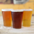 Three disposable glasses of beer on a wooden surface with a blurred background