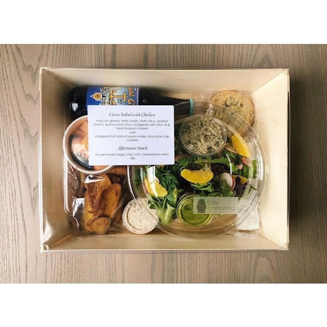 Prepared meal kit with salad, bread, and sauces in a box on a wooden surface
