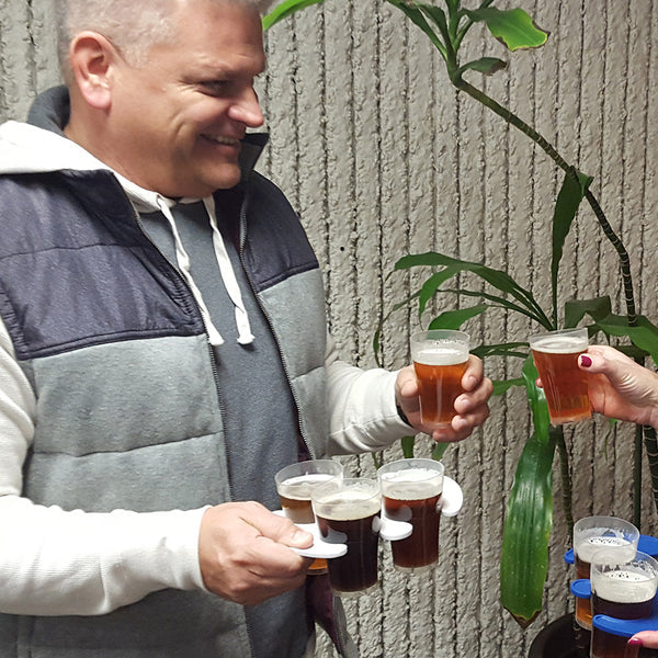 Man holding a compostable cup of beer outdoors with a plant in the background