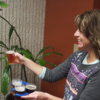 Woman holding a compostable cup of beer next to a tray with more glasses indoors.