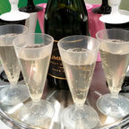 Compostable champagne flutes with champagne on a tray, with a bottle of champagne in the background.